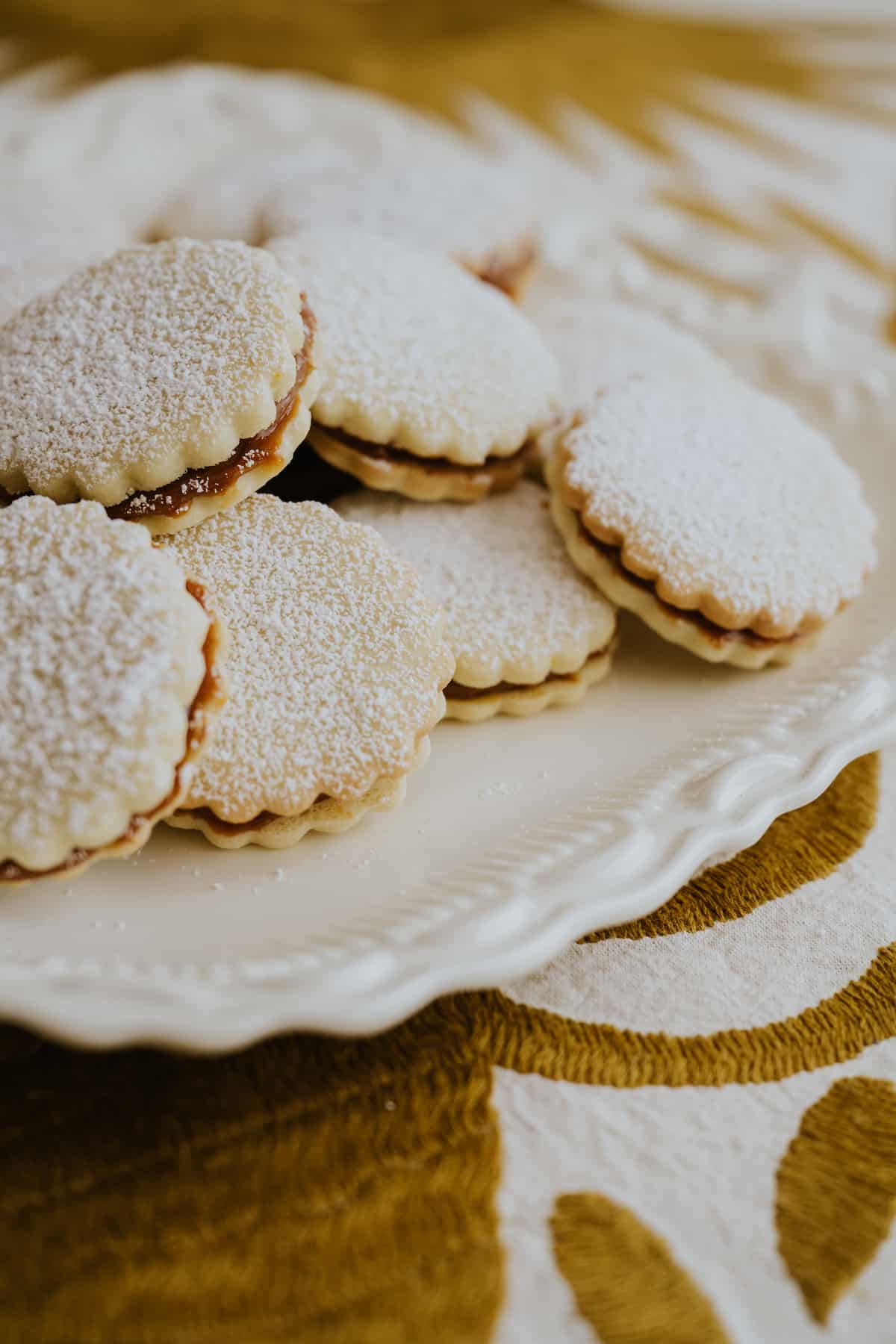 white serving platter of alfajores de maicena sandwich cookies dusted with powdered sugar. 