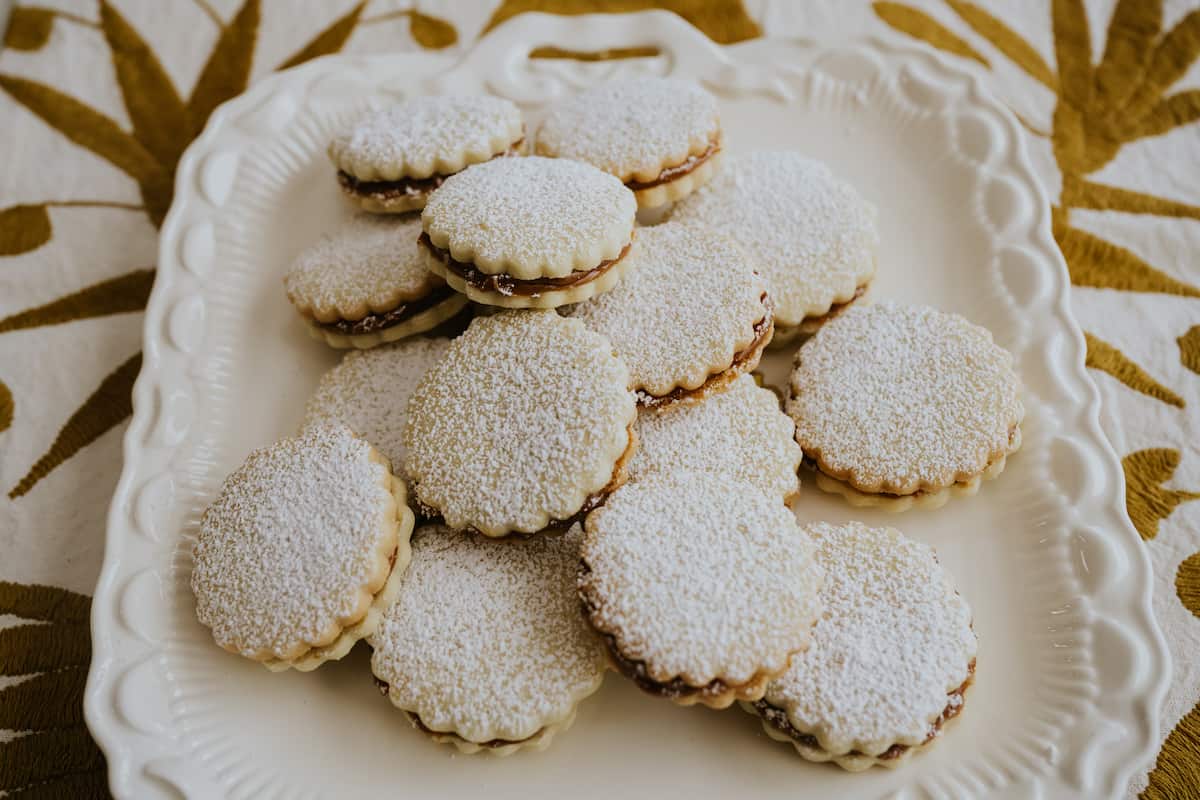rectangular white serving platter filled with powdered sugar-dusted alfajor cookies. 