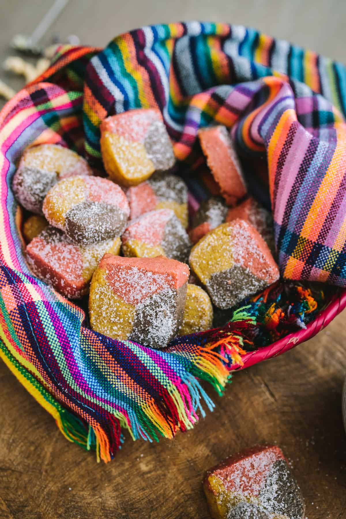 brightly colored basket filled with round and square tri-colored Mexican shortbread cookies known as polvorones. 