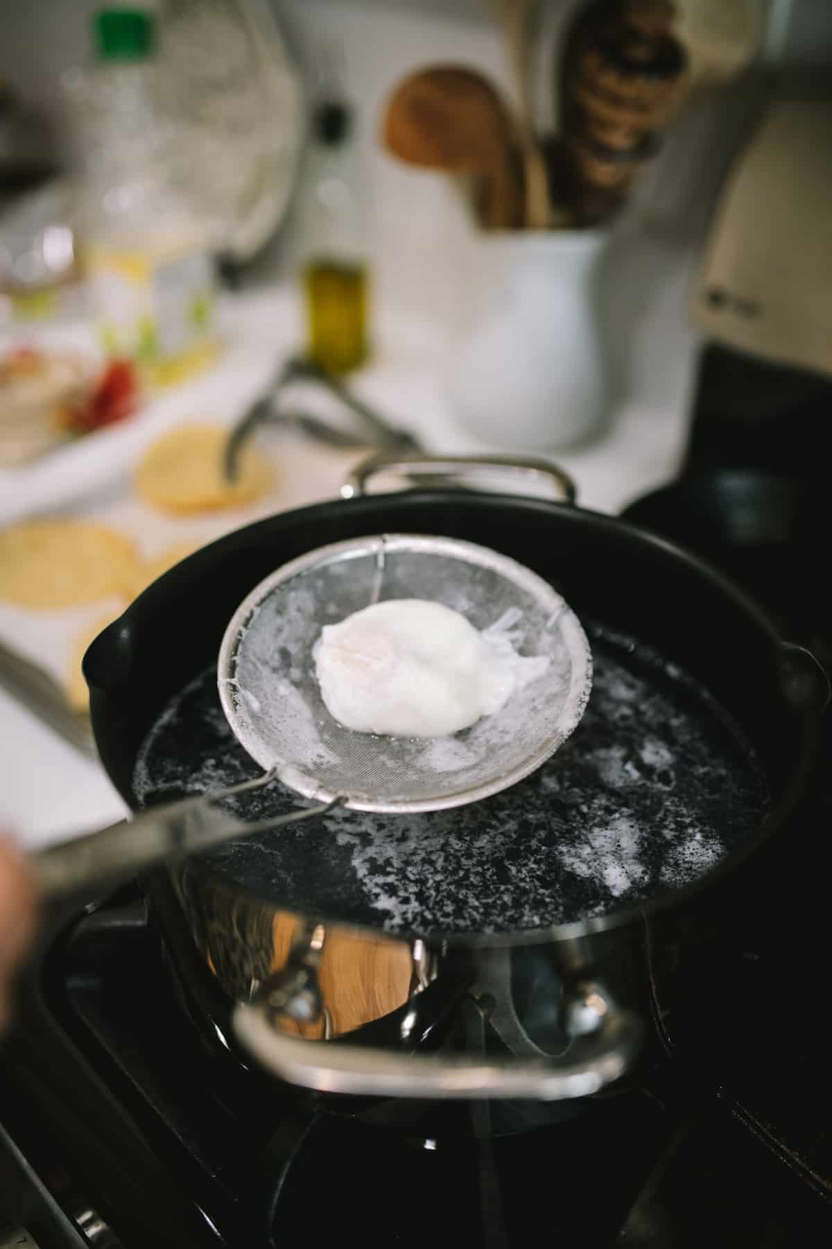 lifting a poached egg out of simmering water using a spider.