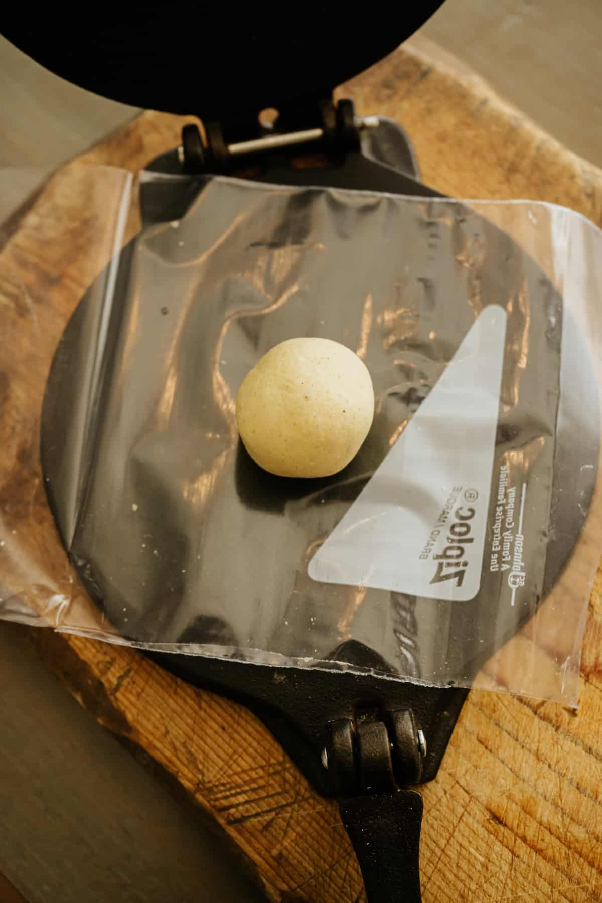 molote dough ball on a halved ziploc bag between the plates of a cast iron tortilla press.