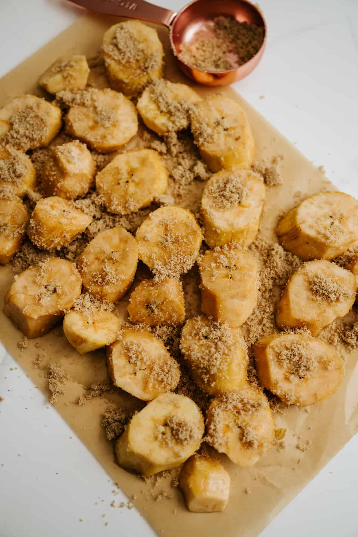 sliced plantains sprinkled with brown sugar on a piece of parchment.