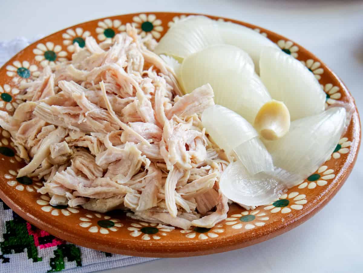 shredded chicken on a terracotta plate with boiled onion quarters and garlic clove.