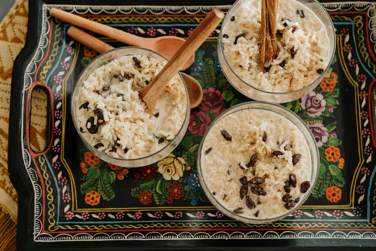 horizontal hero shot of 3 goblets of arroz con leche on a multicolored hand-painted floral serving tray.
