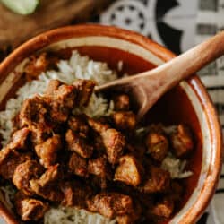 Cuenco de barro mexicano lleno de arroz al vapor y carne adovada, estofado de cerdo al estilo de Nuevo México con chiles rojos sobre una mesa de azulejos estampados en blanco y negro.