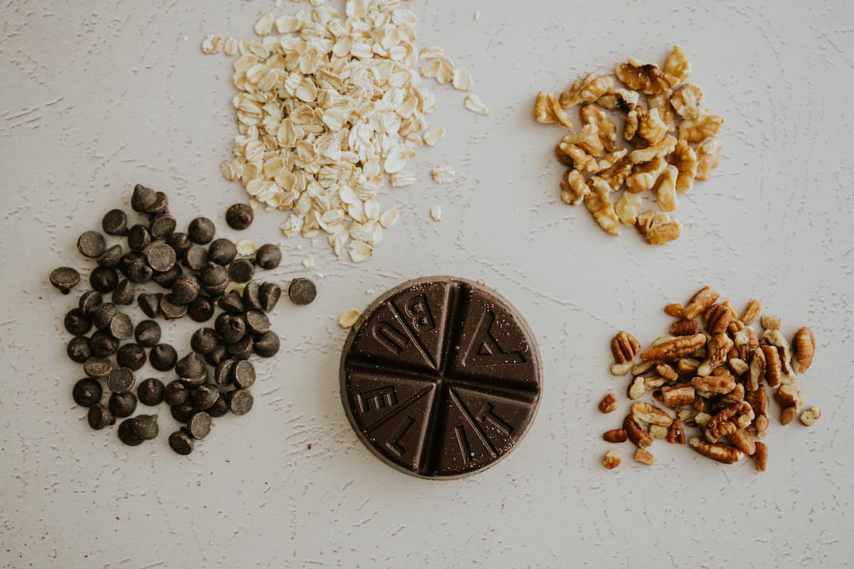 oats, chocolate chips, walnuts, pecans, and a round of Abuelita mexican chocolate on a white table.