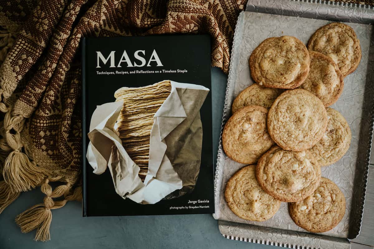 overhead shot of a silver tray of white chocolate chip cookies next to MASA cookbook.