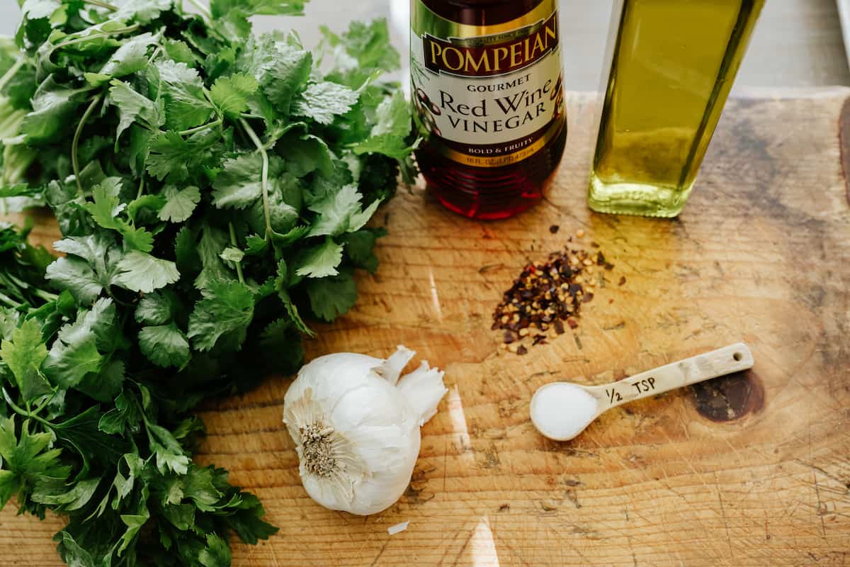 ingredients for making parsley cilantro chimichurri measured out on a wooden cutting board.