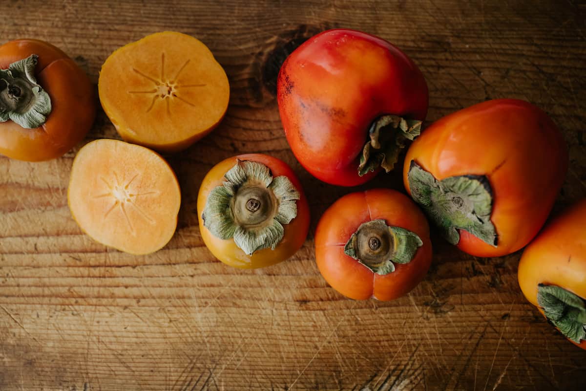 persimmons on a wooden cutting board with one cut in half.