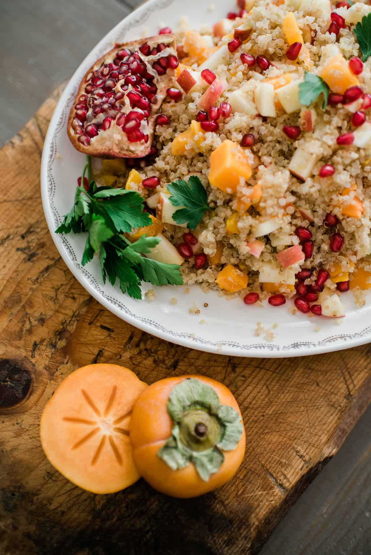 oblong white serving platter filled with roasted butternut squash quinoa salad garnished with a half of a pomegranate and a bunch of parsley.