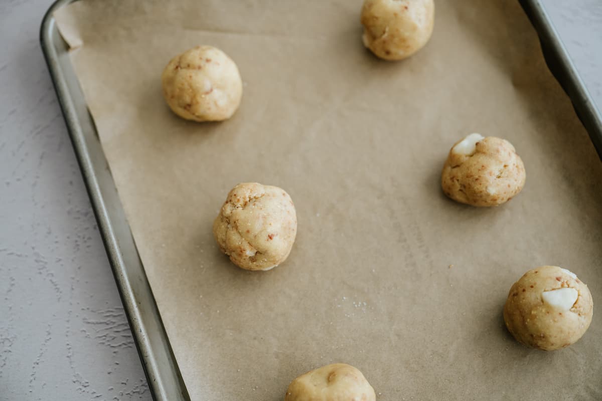 white chocolate chip cookie dough balls on a parchment lined baking sheet.
