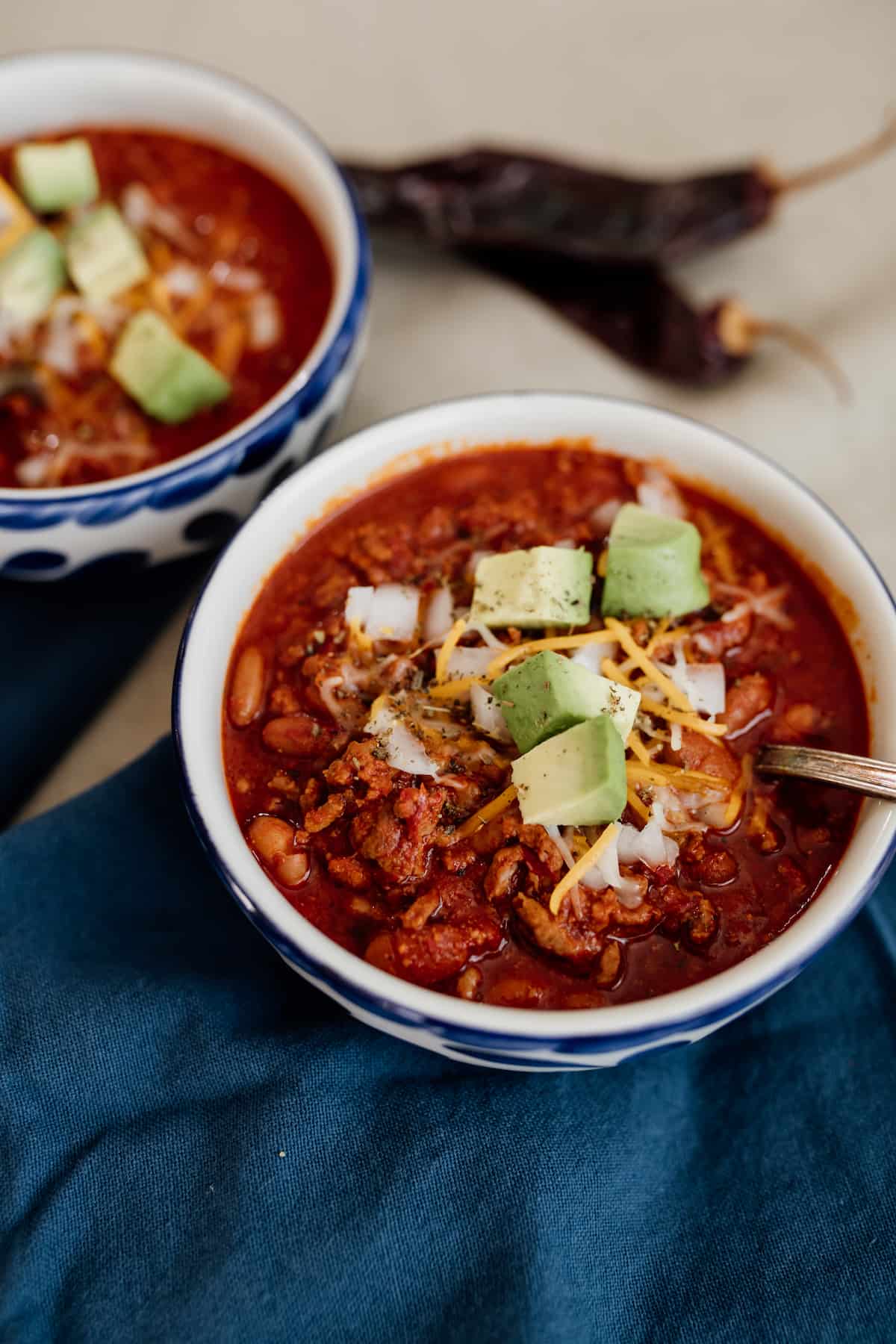 Mexican chili con carne topped with onions, cheese and avocados in blue and white bowls.