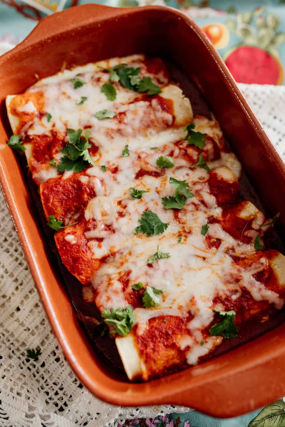 easy red chicken enchiladas in a terra cotta baking dish after baking and topped with cilantro.
