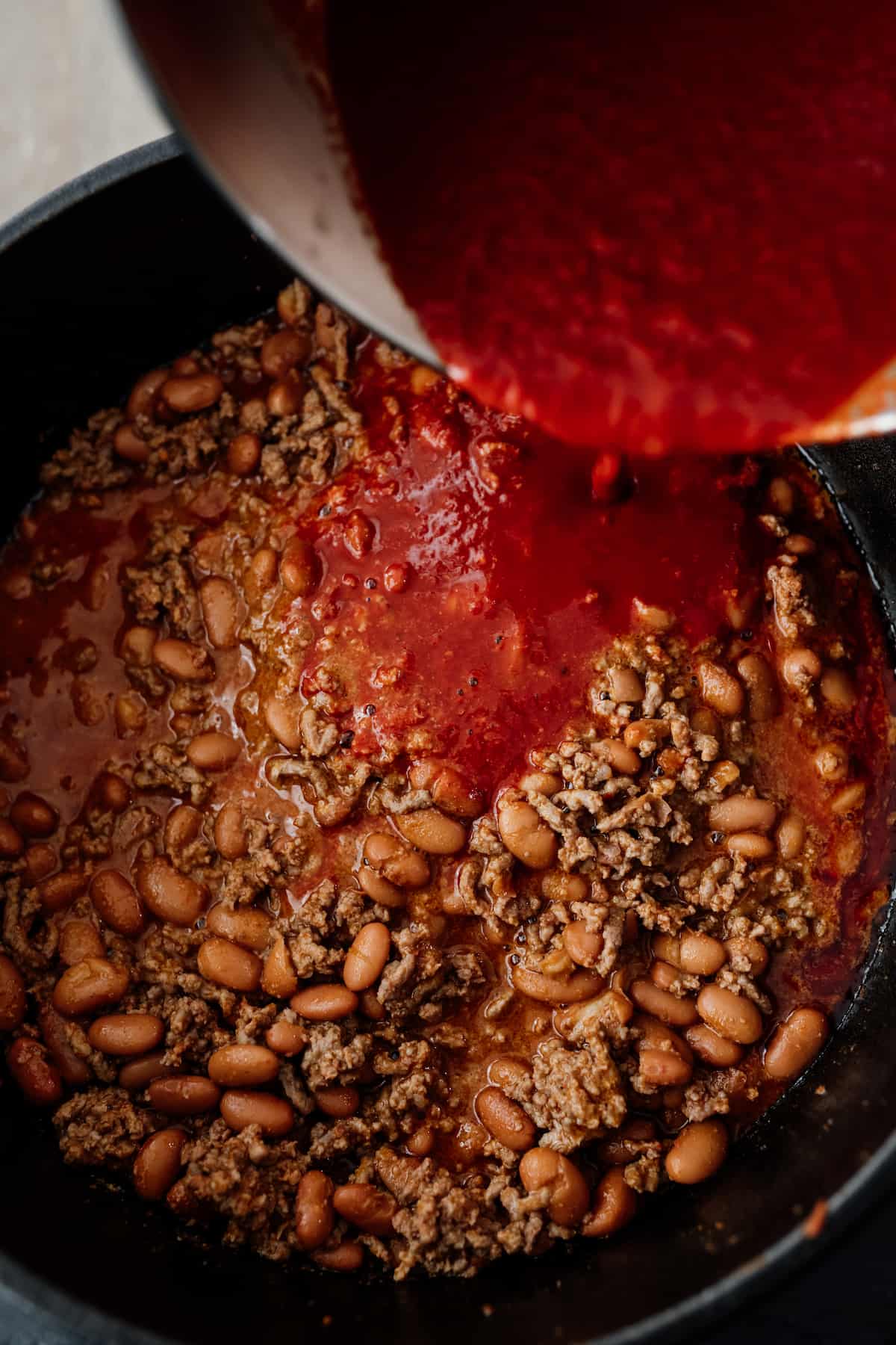 enchilada sauce being added to chorizo chili in a dutch oven.