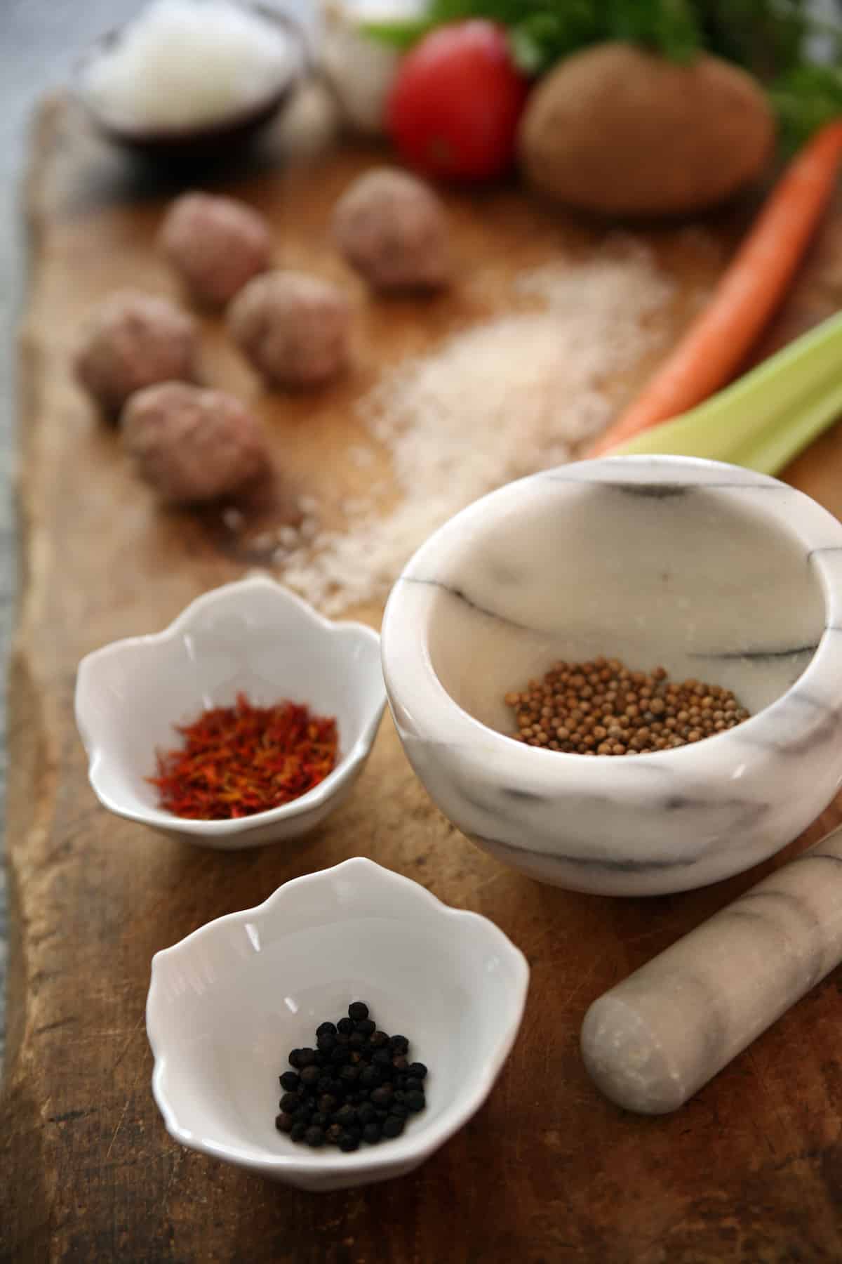 three white bowls of spices on a wooden cutting board to make meatballs albondigas for mexican meatball soup.