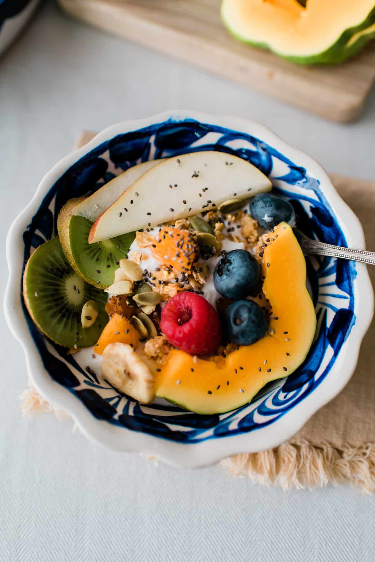 Fotografía cenital de un parfait de yogur casero cubierto con melón, bayas, kiwi, granola, pepitas y semillas de chía.