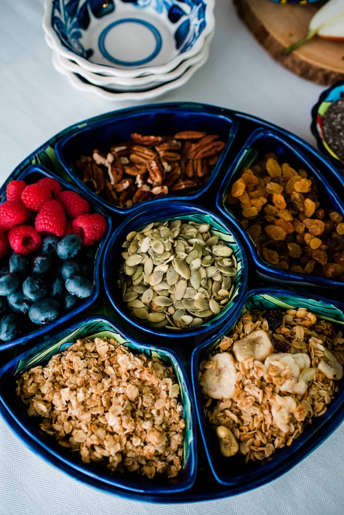 overhead shot of a serving platter with individual bowls of different types of fresh and dried fruit, nuts, and granola for making DIY yogurt parfaits.