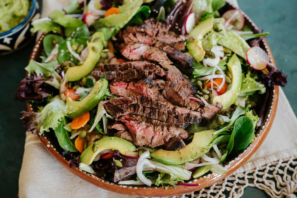 overhead shot of a bowl of carne asada salad topped with thinly sliced flank steak.