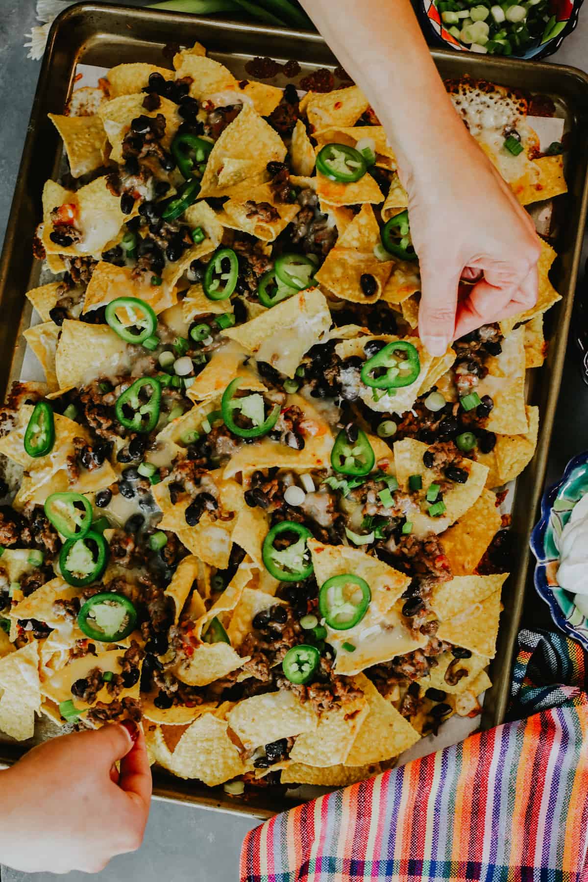 hands pulling baked beef nachos from the sheet pan. 