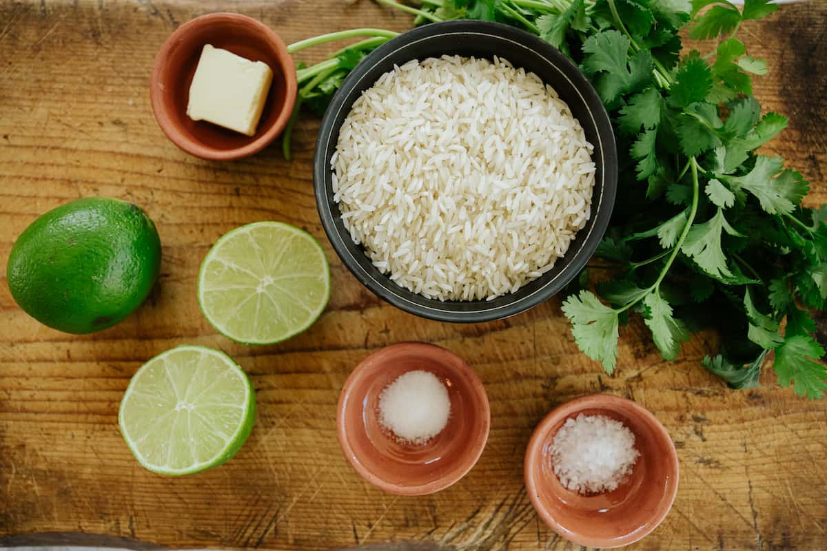 overhead shot of ingredients needed to make cilantro lime rice measured out into bowls on a wooden table.