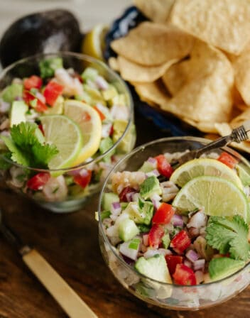 two glass goblets filled with mexican shrimp ceviche de camaron and topped with lemon and lime wedges.